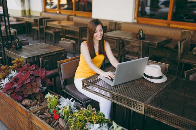 Mulher na rua ao ar livre, café, café, sentada à mesa, trabalhando em um moderno laptop, relaxando no restaurante durante o tempo livre