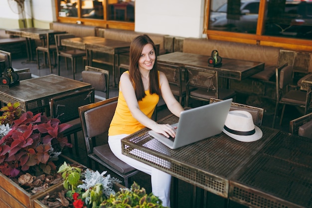 Mulher na rua ao ar livre, café, café, sentada à mesa, trabalhando em um moderno laptop, relaxando no restaurante durante o tempo livre