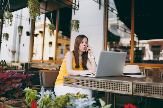 Mulher na rua ao ar livre, café, café, sentada à mesa, trabalhando em um moderno laptop, relaxando no restaurante durante o tempo livre