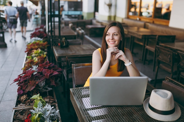 Mulher na rua ao ar livre, café, café, sentada à mesa, trabalhando em um moderno laptop, relaxando no restaurante durante o tempo livre