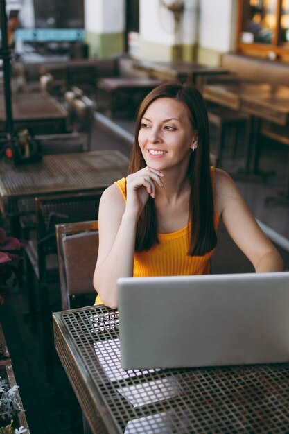 Foto mulher na rua ao ar livre, café, café, sentada à mesa, trabalhando em um moderno laptop, relaxando no restaurante durante o tempo livre