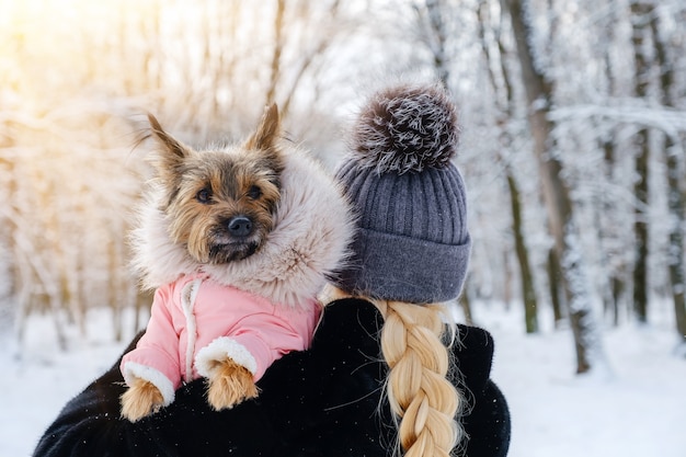Mulher não reconhecida mantém seu cachorro vestido em seus braços no inverno ao ar livre em caminhada. Conceito de cuidados para animais de estimação.
