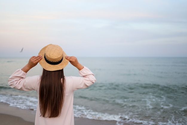 Mulher nas férias de verão usando chapéu de palha e vestido de praia, apreciando a vista para o mar