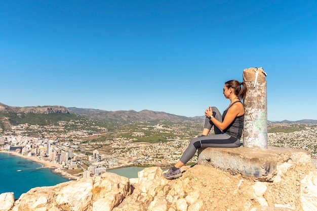 Mulher nas montanhas, sentada em uma rocha, observando a cidade