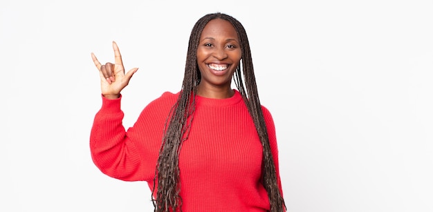 Mulher negra adulta afro se sentindo feliz, divertida, confiante, positiva e rebelde, fazendo sinal de rock ou heavy metal com a mão