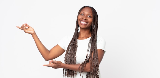 Mulher negra adulta afro sorrindo com orgulho e confiança, sentindo-se feliz e satisfeita e mostrando um conceito no espaço da cópia