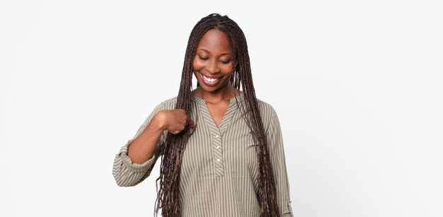 Mulher negra adulta negra sorrindo alegre e casualmente, olhando para baixo e apontando para o peito