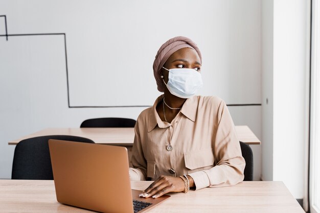 Mulher negra africana com laptop. Uso do computador para trabalho on-line. Máscara médica para proteção contra coronovírus covid-19.