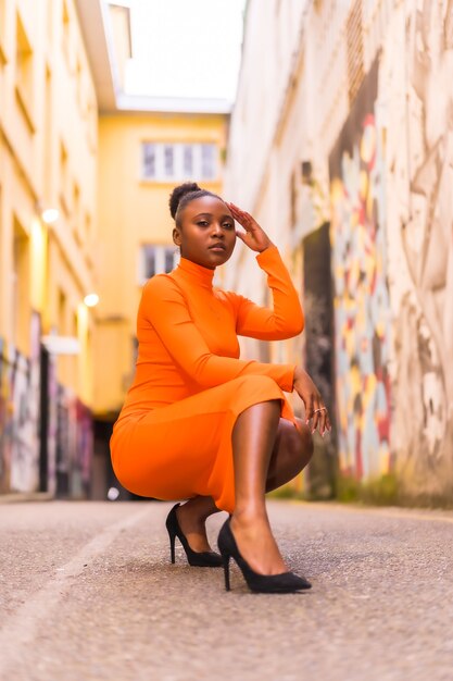 Mulher negra africana com vestido laranja e salto alto em uma rua da cidade