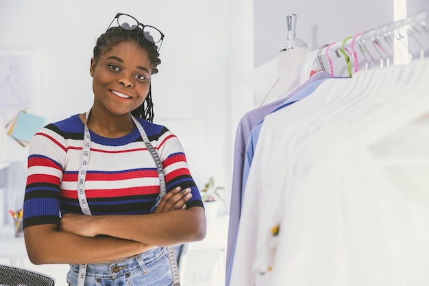 Mulher negra africana feliz figurinista alfaiate designer de roupas feliz trabalhando em estúdio de roupas