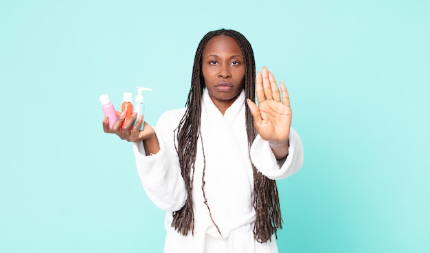 Mulher negra afro-americana adulta vestindo roupão de banho e segurando produtos cosméticos