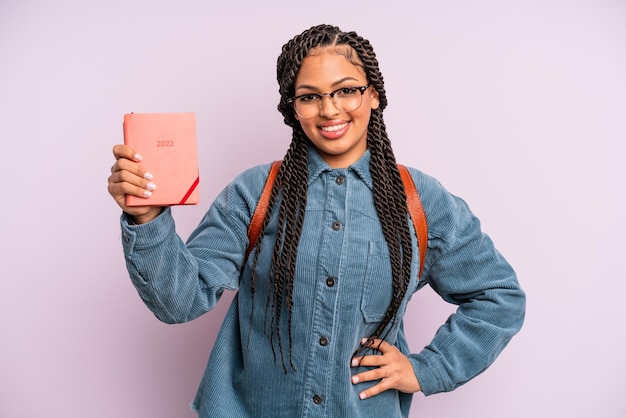 Mulher negra afro sorrindo alegremente com uma mão no quadril e confiante. calendário estudantil ou conceito de agenda