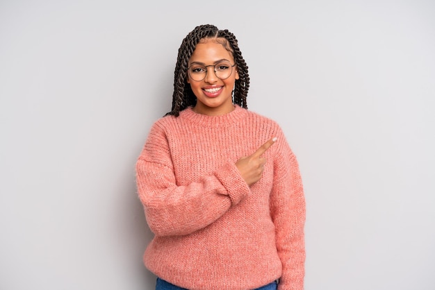 Mulher negra afro sorrindo alegremente, sentindo-se feliz e apontando para o lado e para cima, mostrando o objeto no espaço da cópia