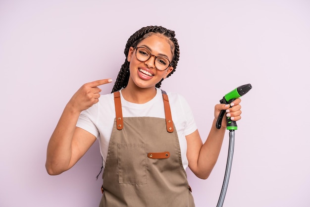 Mulher negra afro sorrindo com confiança apontando para o próprio sorriso largo. conceito de mangueira de jardineiro