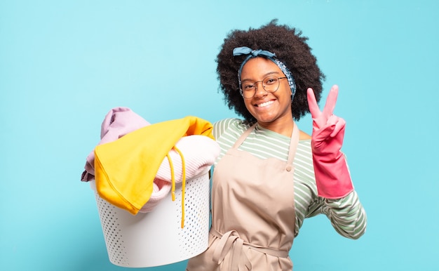 Mulher negra afro sorrindo e parecendo amigável, mostrando o número dois ou o segundo com a mão para a frente, em contagem regressiva. conceito de limpeza. conceito doméstico