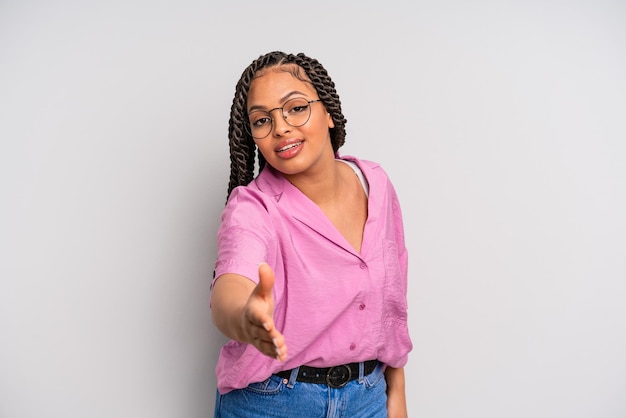 Mulher negra afro sorrindo, parecendo feliz, confiante e amigável, oferecendo um aperto de mão para fechar um acordo, cooperando