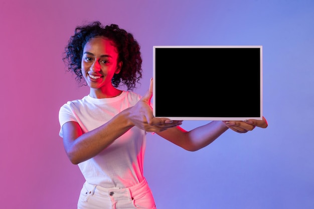 Foto mulher negra alegre segurando um tablet com fundo de gradiente de tela preta