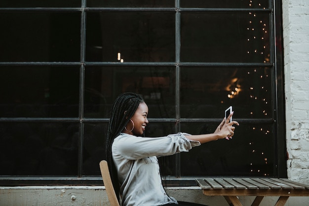 Mulher negra alegre tirando uma selfie em um café ao ar livre