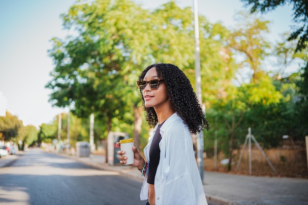 Mulher negra alegre tomando um café de manhã enquanto caminha para o trabalho