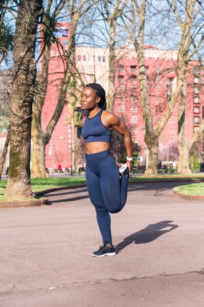 Mulher negra aquecendo e alongando os músculos para iniciar um treinamento físico ou correr em um parque público de rua