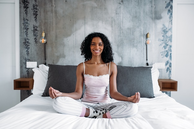Mulher negra atraente na cama meditando