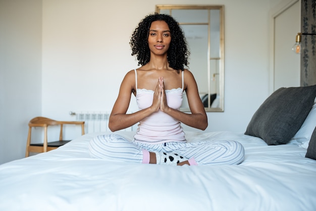 Mulher negra atraente na cama meditando