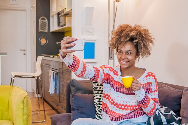 Mulher negra atrativa que toma selfie. Jovem usando um smartphone móvel para tirar fotos de selfies de si mesma em rede em linha em sua casa