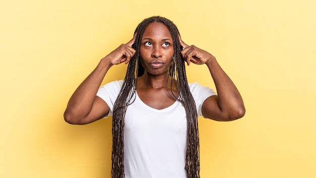 Mulher negra bonita afro se sentindo confusa ou duvidando, concentrando-se em uma ideia, pensando bem, procurando copiar o espaço ao lado