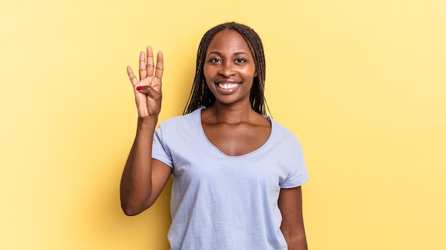 Mulher negra bonita, negra, sorrindo e parecendo amigável, mostrando o número quatro ou o quarto com a mão para a frente, em contagem regressiva