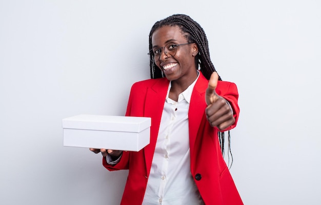 Mulher negra bonita se sentindo orgulhosa, sorrindo positivamente com os polegares para cima. empresária com uma caixa branca