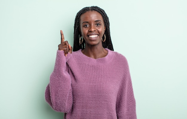 Mulher negra bonita sorrindo alegre e feliz, apontando para cima com uma das mãos para copiar o espaço