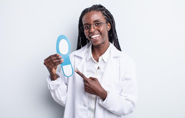 Mulher negra bonita sorrindo alegremente, sentindo-se feliz e apontando para o lado. conceito de podólogo