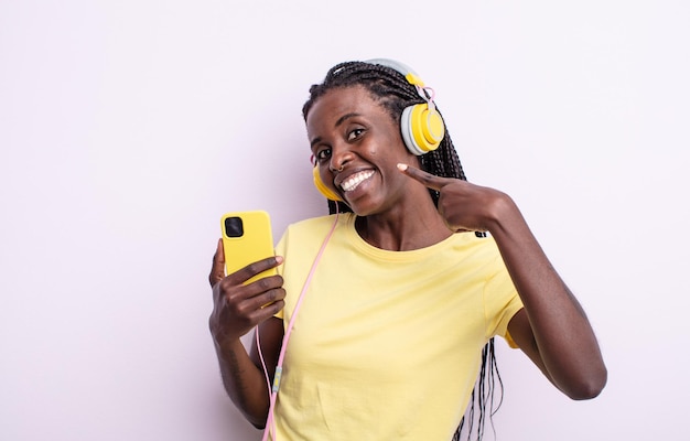 Mulher negra bonita sorrindo com confiança apontando para o próprio sorriso largo. ouvindo o conceito de música