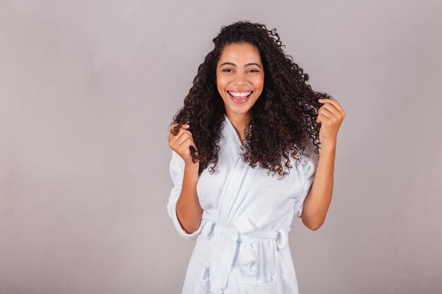 Foto mulher negra brasileira vestindo roupão e toalha de cabelo encaracolado spa centro de beleza cuidados com os cabelos mostrando cachos de cabelo