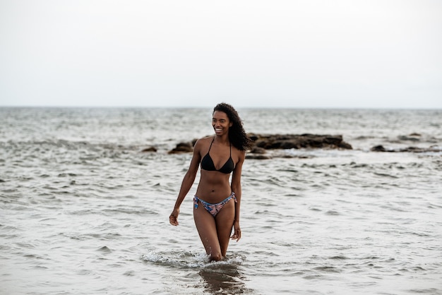 Mulher negra brincalhona e bonita de biquíni em uma praia vulcânica em Santo Antão, Cabo Verde