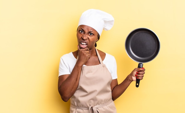 Mulher negra chef afro com boca e olhos bem abertos e mão no queixo, sentindo-se desagradavelmente chocada, dizendo o quê ou uau