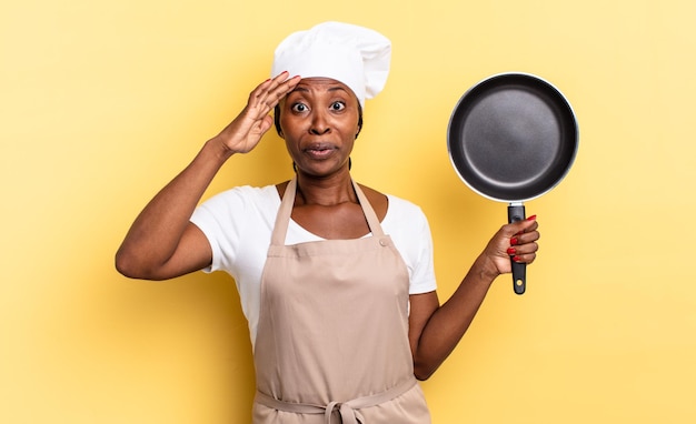 Mulher negra chef afro parecendo feliz, atônita e surpresa, sorrindo e dando uma boa notícia incrível