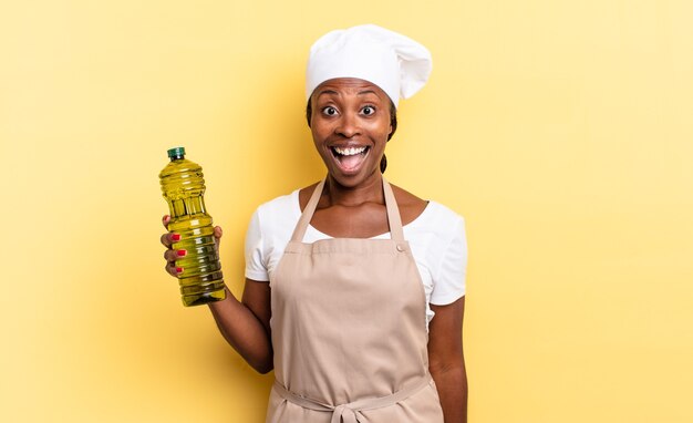 Mulher negra chef afro parecendo muito chocada ou surpresa, olhando com a boca aberta e dizendo uau. conceito de azeite