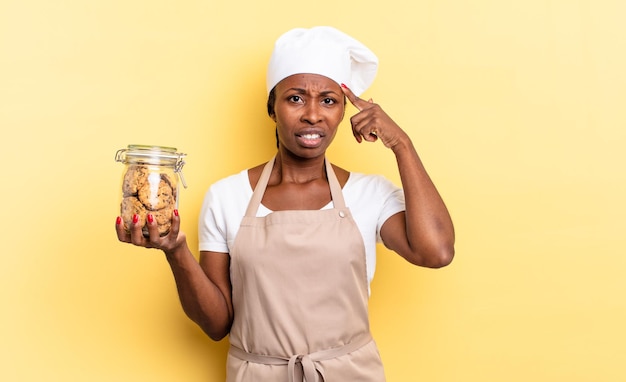 Mulher negra chef afro se sentindo confusa e confusa, mostrando que você é louco, louco ou louco. conceito de biscoitos
