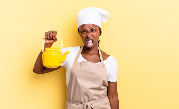 Mulher negra chef afro se sentindo enojada e irritada, mostrando a língua, não gostando de algo desagradável e nojento. conceito de bule