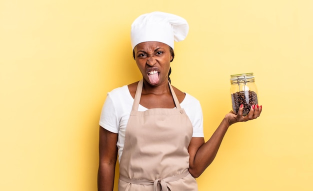 Mulher negra chef afro se sentindo enojada e irritada, mostrando a língua, não gostando de algo desagradável e nojento. conceito de grãos de café