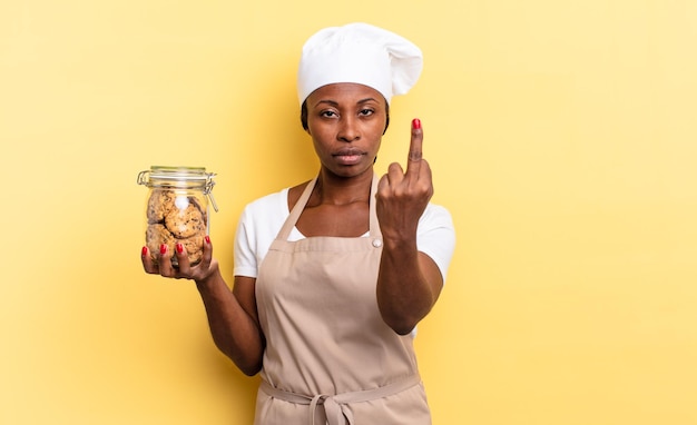 Mulher negra chef afro se sentindo zangada, irritada, rebelde e agressiva, virando o dedo médio, revidando. conceito de biscoitos