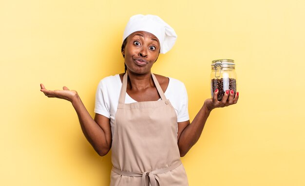 Mulher negra chef afro sentindo-se perplexa e confusa, duvidando, ponderando ou escolhendo diferentes opções com expressão engraçada. conceito de grãos de café