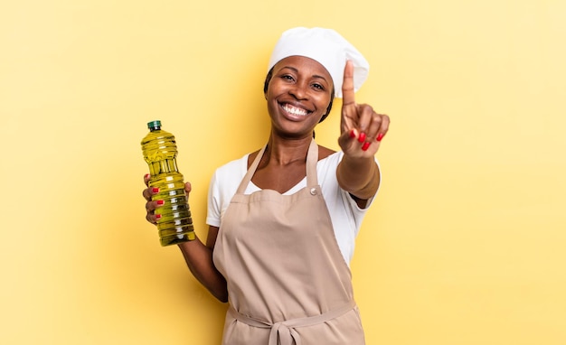 Mulher negra chef afro sorrindo com orgulho e confiança, fazendo a pose número um triunfante, sentindo-se como um conceito líder de azeite