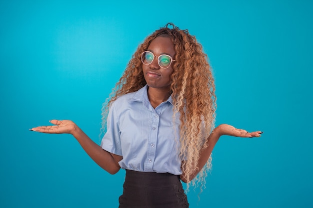 Mulher negra com cabelo encaracolado em foto de estúdio, vestindo camisa azul e saia preta e fazendo várias expressões faciais.