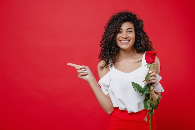 Foto mulher negra com rosa na mão, apontando o dedo no espaço da cópia isolado sobre o vermelho