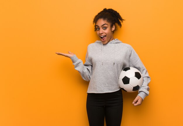 Mulher negra de aptidão jovem segurando algo com a mão. segurando uma bola de futebol.