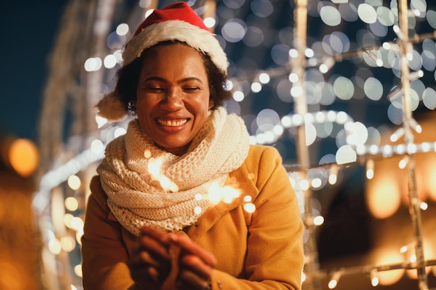 Mulher negra de meia-idade segurando estrelinhas na noite festiva de inverno na cidade.