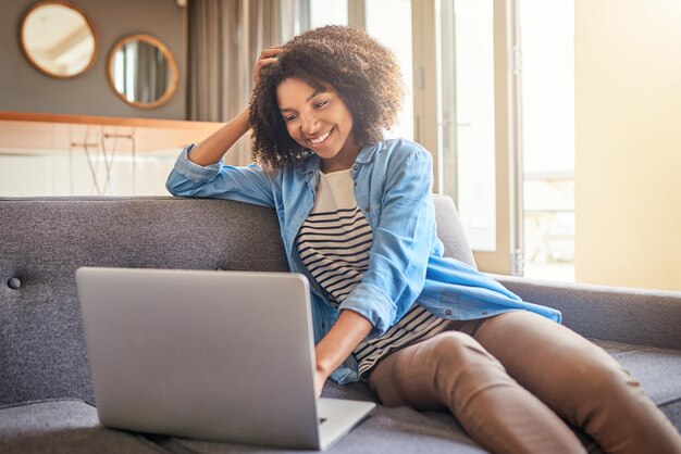 Foto mulher negra de tecnologia com laptop e no sofá de sua sala de estar em sua casa sorrindo mídia social ou rede de conectividade e mulher africana lendo um e-mail em seu dispositivo digital no sofá