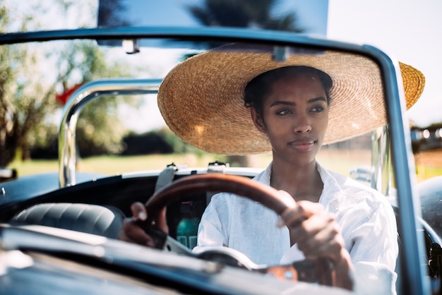 Mulher negra, dirigindo um carro conversível antigo